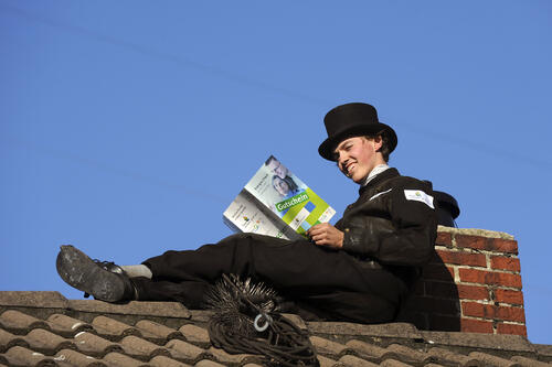 Schornsteinfeger liest Gutschein auf Dach 